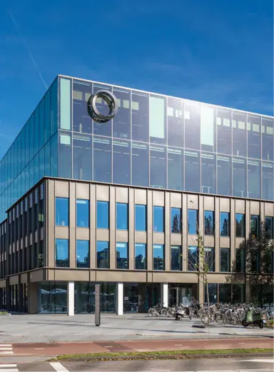 Modern office building with reflective glass facade and a circular logo on the upper story, situated under a clear blue sky. The ground level features large windows, private office spaces, and a bike rack full of An image from EDGE Workspaces.